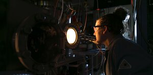 A woman in a lab coat is looking at glowing instruments in a lab