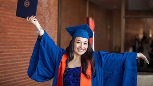 A female student in graduationg regalia spreads her arms holding a diploma