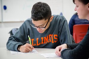 A female teaching assistant helps a male undergraduate student with an assignment during class.