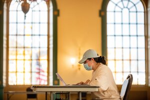student with a mask studying in a lounge. 